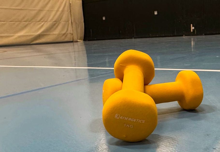 Hanteln Herzsportgruppe Kirn Gelbe Hanteln liegen auf einem blauen Boden in einer Sporthalle.